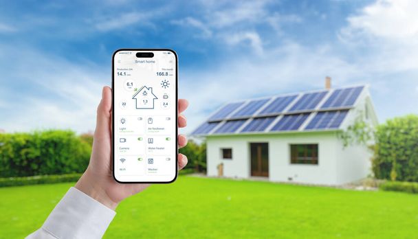 Рука тримає смартфон із додатком "розумний дім", стежить за енергією, температурою та споживанням енергії на сонячній панелі, просуваючи концепцію ефективного зеленого життя - Фото, зображення