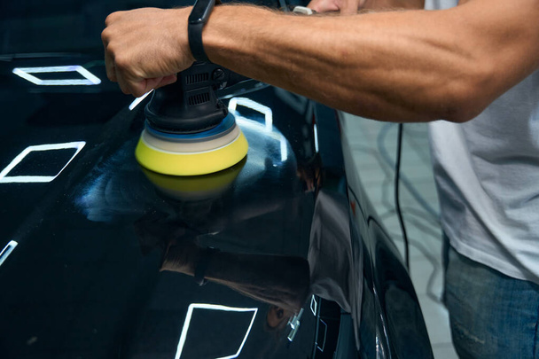 Detailing a modern car in a car repair shop, the master has muscular arms - Foto, Bild