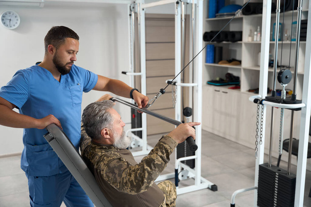 Experienced physiotherapist works with a patient in the gym, a specialist uses a special simulator - Fotoğraf, Görsel