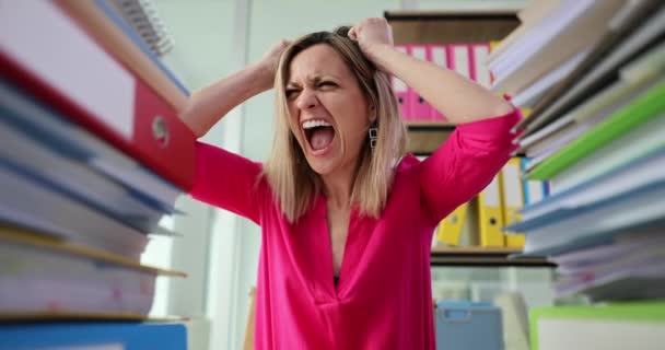 Businesswoman screaming and pulling out hair near many folders with paper documents 4k movie slow motion. Problems of organizing paperwork concept - Materiał filmowy, wideo
