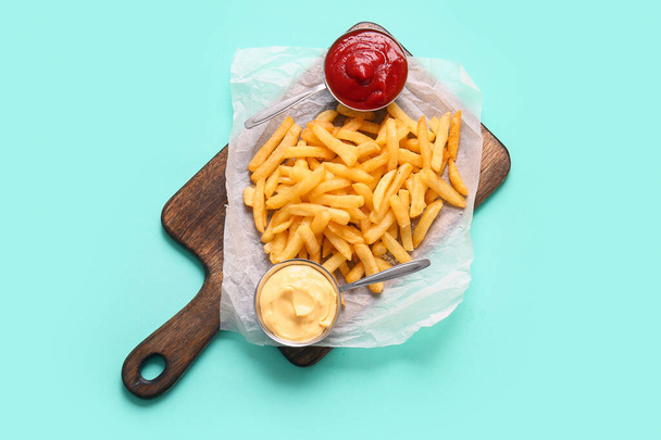 Houten plank met lekkere frietjes en sauzen op kleur achtergrond - Foto, afbeelding