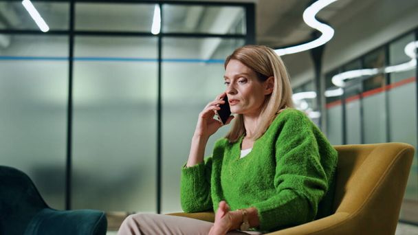 Μια σίγουρη επιχειρηματίας που μιλάει στο εσωτερικό του γραφείου. Κοντινό πλάνο γυναίκα διευθυντής καλώντας το κινητό τηλέφωνο σε πολυθρόνα θέση. Σοβαρή ξανθιά διευθύντρια έχει τηλεφωνική συνομιλία. Σχέδιο επιχειρηματικής συνομιλίας - Φωτογραφία, εικόνα