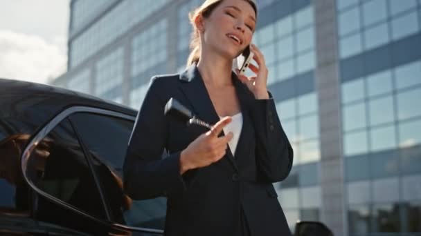 Succès vendeur de voiture appelant sur le jeu de rue avec les clés à la main zoom arrière. Heureuse femme d'affaires parlant smartphone s'appuyant sur l'auto premium. Élégante dame acheteur d'automobiles parlant téléphone portable - Séquence, vidéo