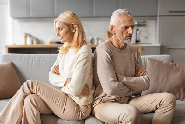 Upset senior married couple grey-haired man and blonde woman sit back to back on couch at home, not talk to each other, feeling down after fight, have difficulties in marriage, thinking about divorce - Foto, afbeelding