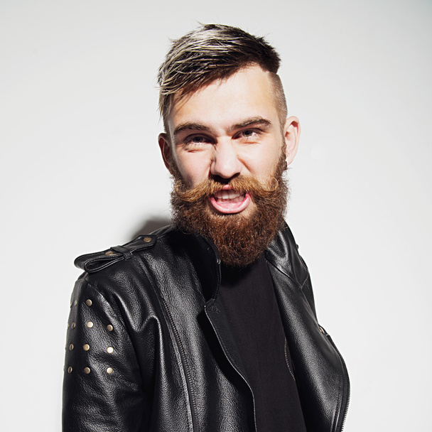 Emotional portrait of a bearded young man in a leather jacket in the studio - Фото, изображение
