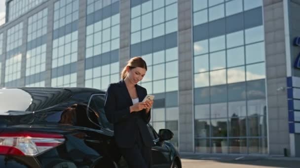 Happy business woman texting on cellphone leaning at luxury car outdoors zoom in. Elegant lady smiling looking on smartphone screen at street. Satisfied businesswoman reading phone message close up. - Footage, Video