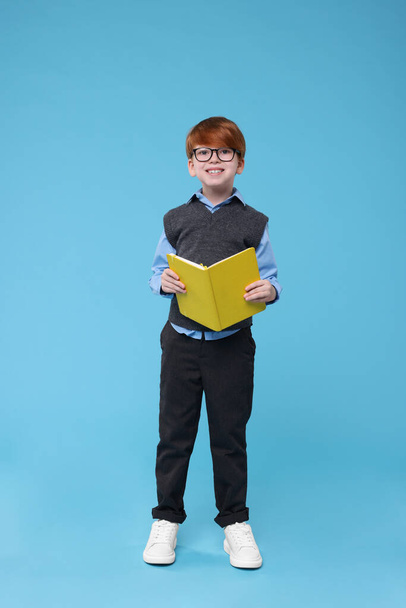 Smiling schoolboy in glasses with book on light blue background - Фото, изображение