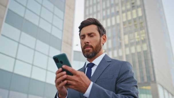 Financial manager browsing app looking smartphone screen on go close up. Confident businessman reading report at cellphone walking on business meeting. Bearded handsome boss typing email on cell phone - Footage, Video