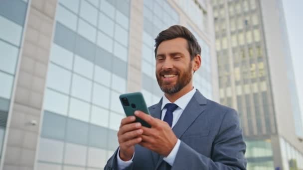 Relaxed employee browsing social media at cellphone walking home after office work close up. Bearded handsome smiling looking at smartphone screen on go. Happy worker reading salary bank notification. - Footage, Video