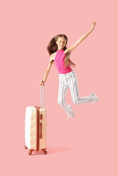 Happy little girl with suitcase jumping on pink background - Fotó, kép