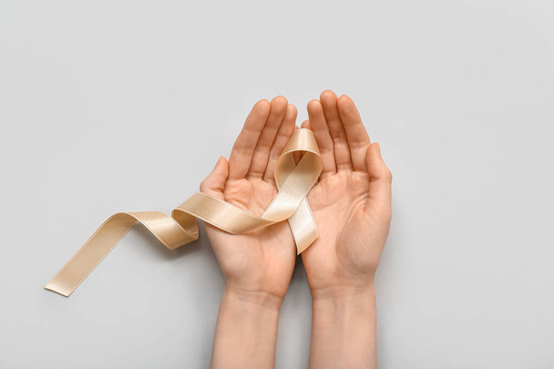 Woman with beige ribbon on light background. Uterine cancer awareness concept - Photo, Image