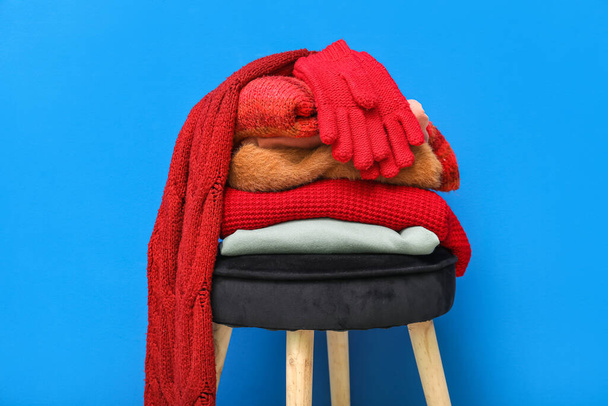 Stack of folded sweaters with scarf and gloves on chair against blue background - Foto, Imagem