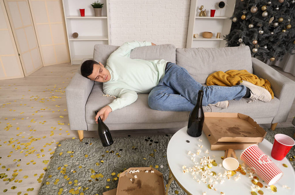 Drunk young man with champagne sleeping on sofa after New Year party at home - Valokuva, kuva