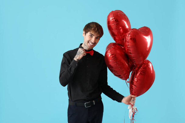 Handsome young man with heart-shaped air balloons for Valentine's day on blue background - Fotografie, Obrázek