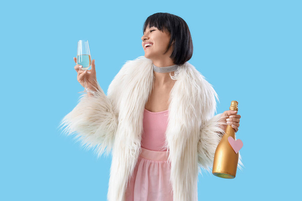 Beautiful young woman with bottle and glass of champagne on blue background. Valentine's day celebration - Fotografie, Obrázek