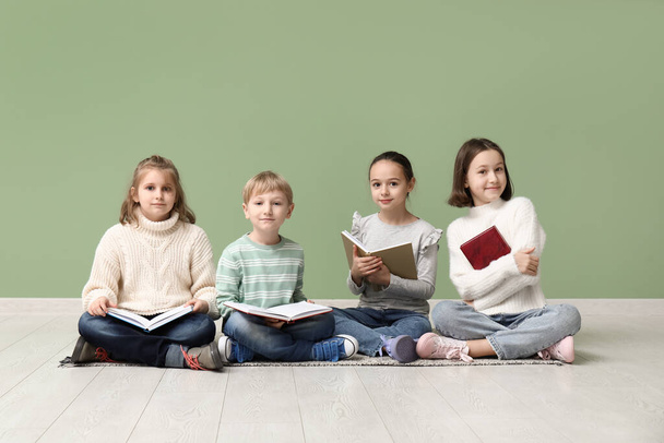 Little children reading books while sitting on floor near green wall - Foto, Imagem