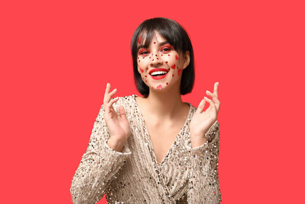 Beautiful happy young woman with creative makeup for Valentines Day on red background - Photo, Image