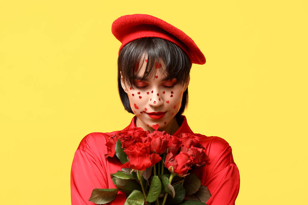 Beautiful young woman with creative makeup for Valentines Day and bouquet of roses on yellow background - Foto, imagen