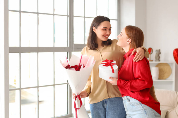 Young lesbian couple with gift and roses at home on Valentine's Day - Photo, Image