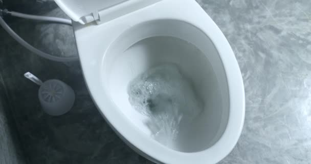 Toilet doorspoelen in de badkamer. Wit keramisch schoon toilet spoelt water door, toiletdeksel sluit langzaam en voorzichtig. Grijze badkamer wc verdieping. Water spoelt naar beneden. Spoelwater in keramisch modern toilet. - Video