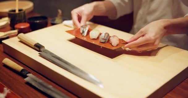 Kädet, sushi lautasen ja esityksen ravintolassa pöydällä ruokapöydässä, ruokaa tai asiantuntija ruoanlaitto yöllä. Henkilö, keittiö tai kala catering, valmis ja palvelu ravitsemus, ruokavalio tai välipala Japanissa. - Materiaali, video