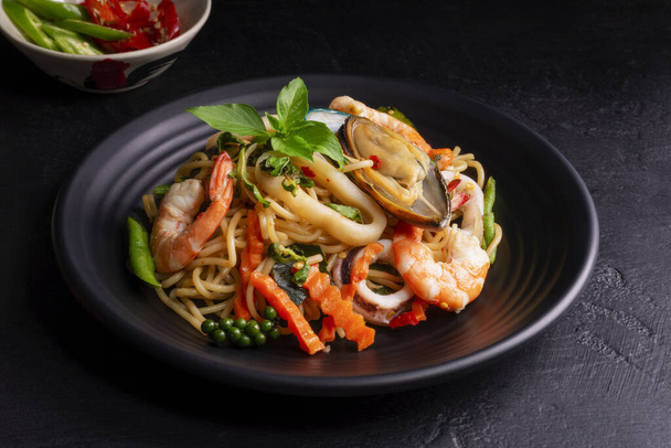 Meeresfrüchte getrunkene Spaghetti mit Shrimp-Tintenfischmuscheln Chili und Basilikum. Thai-Essen. Gesunde Asiatin auf einem Teller auf schwarzem Hintergrund. Ansicht von oben. - Foto, Bild