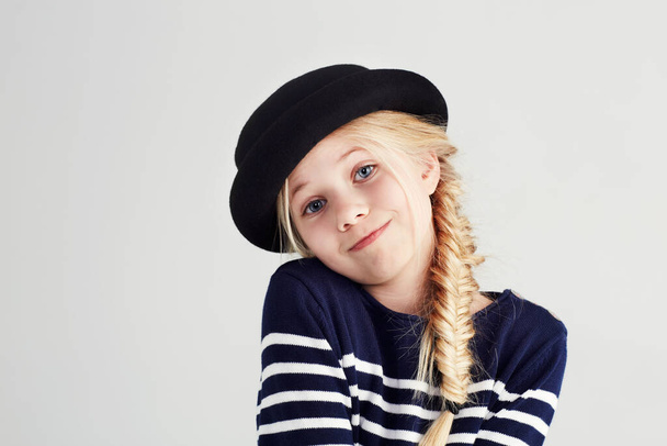 Fashion, smile and portrait of child in a studio with casual, cool and stylish outfit and hat. Happy, youth and young girl kid with positive, good and confident attitude for style by white background. - Photo, Image