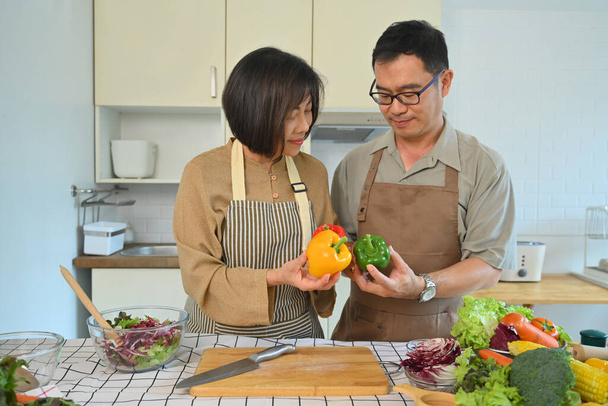 Aufnahme eines glücklichen Senioren-Paares, das in der Küche eine gesunde vegetarische Mahlzeit zubereitet. Gesunder Lebensstil - Foto, Bild