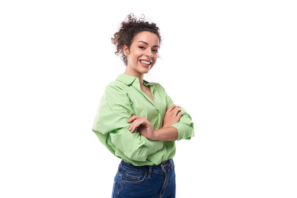 giovane donna d'affari bruna positiva con i capelli ricci legati in una coda di cavallo in una camicia verde chiaro in uno spazio studio. - Foto, immagini