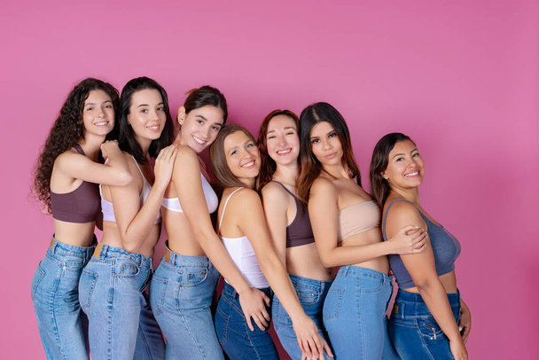 A lineup of seven joyful women in casual denim against a pink background, sharing a moment of happiness.  - Valokuva, kuva