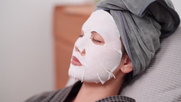 An Asian woman is applying a face mask for a rejuvenating skincare routine, nurturing her skins health and radiance at her home. Capture the essence of self-care and wellness - Felvétel, videó
