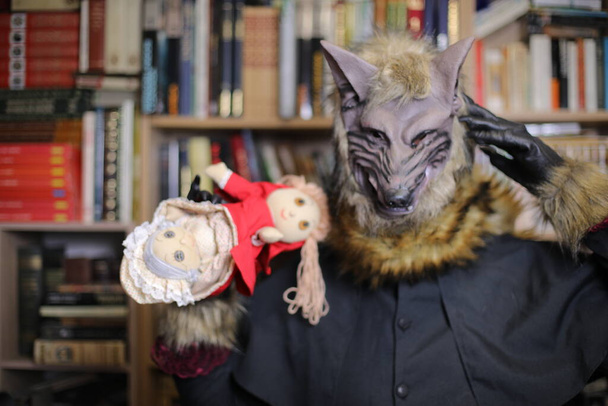 κοντινό πλάνο του ατόμου με μάσκα λύκου στο σπίτι με κόκκινο παιχνίδι κουκούλα - Φωτογραφία, εικόνα