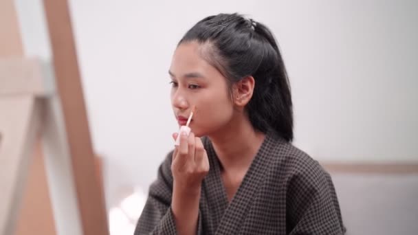 Asian woman applying concealer on her face in front of a large mirror after washing and styling her hair at home. Capture her beauty routine. High quality 4k footage - Záběry, video