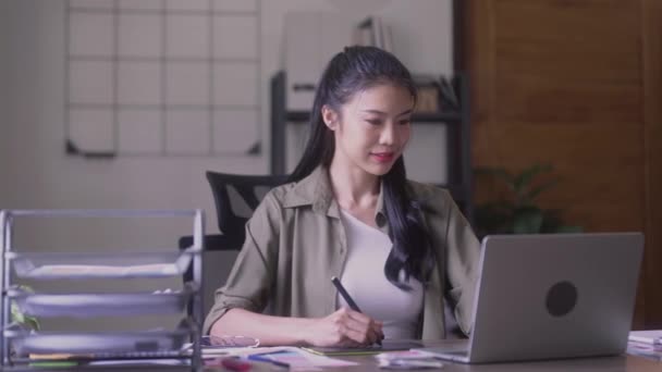 Young Asian Women Graphic designer Artist work on computer laptop and with graphic interactive drawing pen sitting in front of window at desk in office. High quality 4k footage - Footage, Video