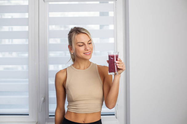 Gezond voedsel concept. Millennial vrouw in sportkleding met glas verse smoothie thuis, ruimte voor tekst - Foto, afbeelding