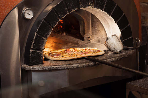 Un horno de piedra irradia calor cuando un chef recupera una pizza adornada con queso derretido y ricos ingredientes, listo para servir - Foto, imagen