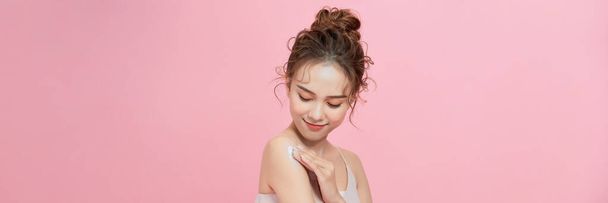  Mujer joven aplicando crema corporal sobre el hombro sobre fondo rosa - Foto, Imagen
