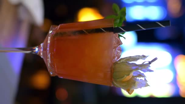Copa de cóctel con zumo de naranja y vodka en un restaurante con luces de neón por la noche - Imágenes, Vídeo