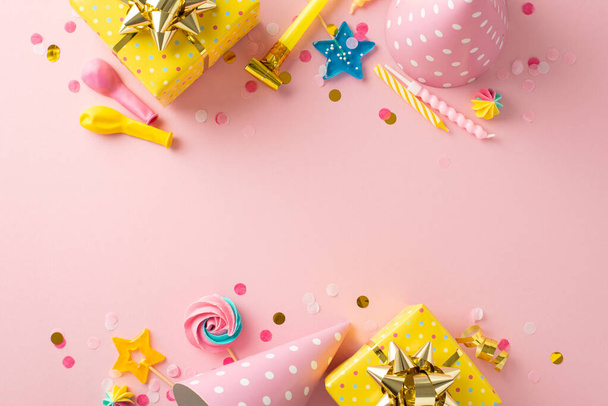 Очаровательная вечеринка. Верхний вид ликующего стола с праздничными элементами, такими как подарочные пакеты, шляпы для вечеринок, леденцы, свечи, воздушные шары, конфетти на пастельно-розовой поверхности - Фото, изображение