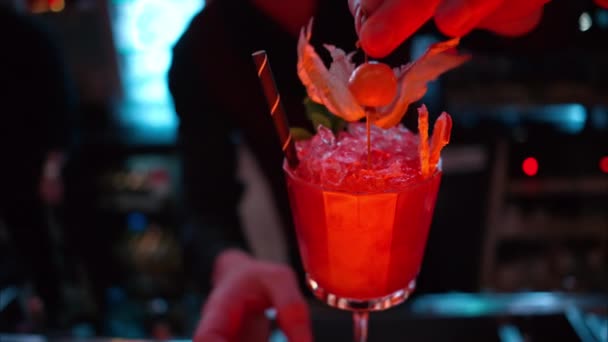 Barmen gece vakti neon ışıkları olan bir barın üzerine buzlu turuncu kırmızı alkol kokteyli döküyor. - Video, Çekim