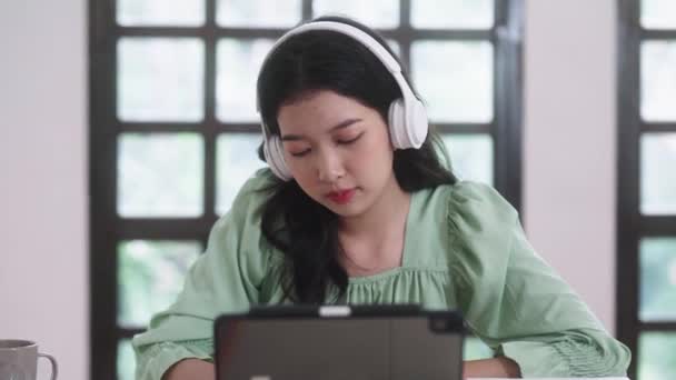 Jeune étudiante asiatique en ligne leçon e-learning avec tablette numérique et écouteurs dans le salon à la maison, concept d'enseignement à distance. Images 4k de haute qualité - Séquence, vidéo