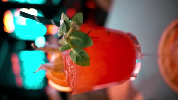 Chiudete il cocktail all'arancia con alcool rosso e ghiaccio in un bar con luci al neon di notte - Filmati, video