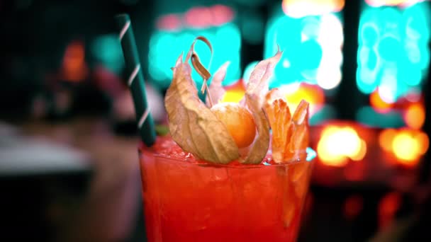 Sluiten oranje rood alcohol cocktail met ijs op een bar met neon lichten 's nachts - Video