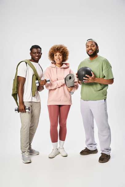 ヨガマット,ボール,ダンベルを持っている幸せなアフリカ系アメリカ人の友人は,灰色の背景,ウェルネスに - 写真・画像