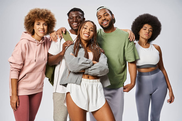 mujer afroamericana feliz posando cerca de amigos en ropa deportiva sobre fondo gris, Juneteenth - Foto, Imagen