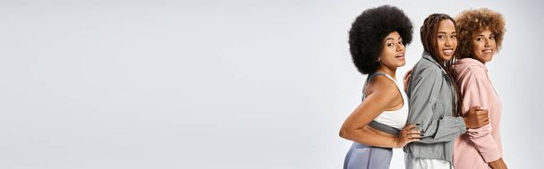 šťastné africké americké přítelkyně ve sportovním oblečení pózují na šedém pozadí, červen 19. prapor - Fotografie, Obrázek