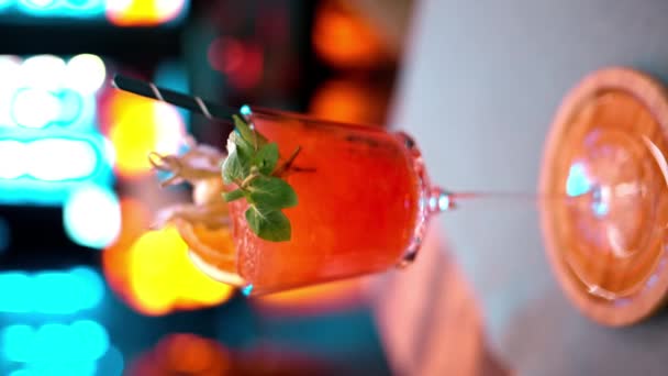 Zavřít oranžový červený alkoholový koktejl s ledem na baru s neonovými světly v noci - Záběry, video