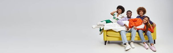 felice donna afroamericana con dreadlocks sdraiato sulle ginocchia di amici sul divano giallo, striscione - Foto, immagini