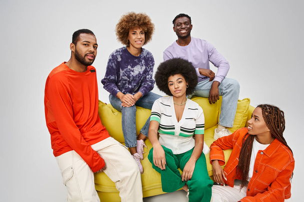 щаслива афроамериканська громада в яскравому повсякденному одязі, сидячи разом на жовтому дивані на сірому - Фото, зображення