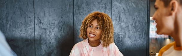 giovane ed elegante receptionist afroamericana sorridente vicino agli studenti in ostello della gioventù, banner - Foto, immagini